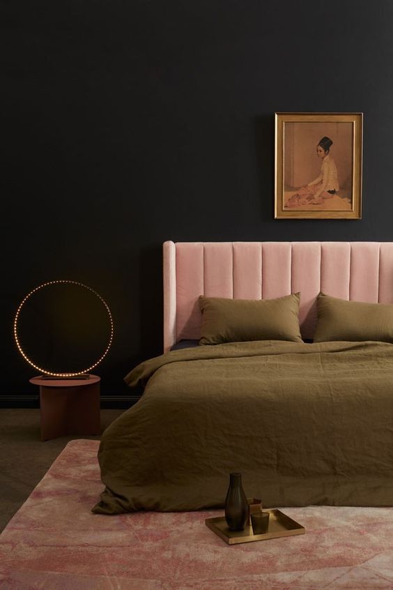 a moody and refined bedroom with black walls, a blush bed, a vintage artwork, green bedding, a bold table lamp