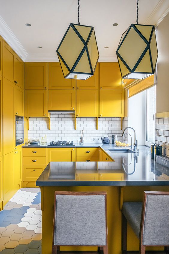 a mustard kitchen with grey stone countertops and grey stools, a white subway tile backsplash anbd geometric pendant lamps