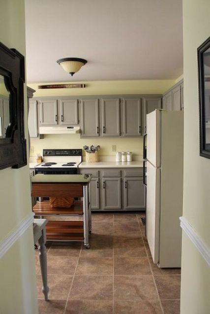 a peaceful kitchen with pale yellow walls, traditional grey cabinets with paneling and a metal and wood kitchen