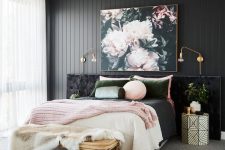 a refined bedroom with a black wooden accent wall, a black upholstered bed, pink and green bedding and a beautiful floral artwork