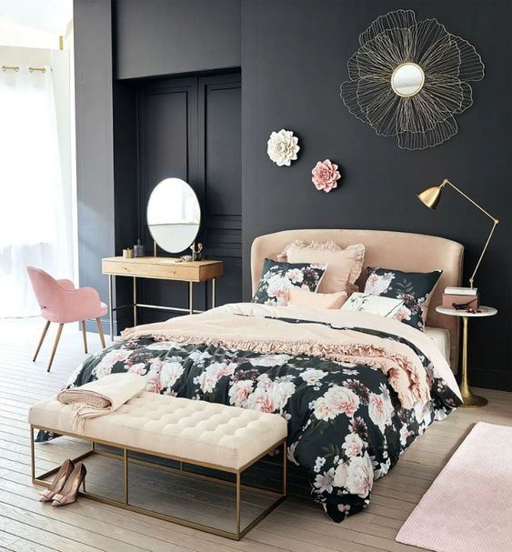 a refined bedroom with black walls, a tan bed and a creamy bench, a pink chair and floral bedding