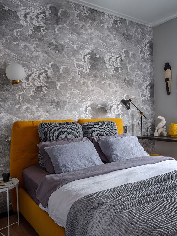 a small bedroom with a grey cloud wallpaper wall, a mustard upholstered bed and accessories, grey and white bedding
