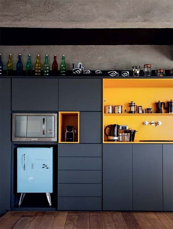 a small built in graphite grey kitchen with a yellow niche for storage and a powder blue mini fridge
