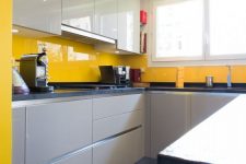 a stylish minimalist kitchen with white and dove grey cabinetry and a sunny yellow sleek glass backsplash stands out