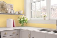 an airy kitchen with light yellow walls, dove grey cabinets and shelves, white pendant lamps and countertops