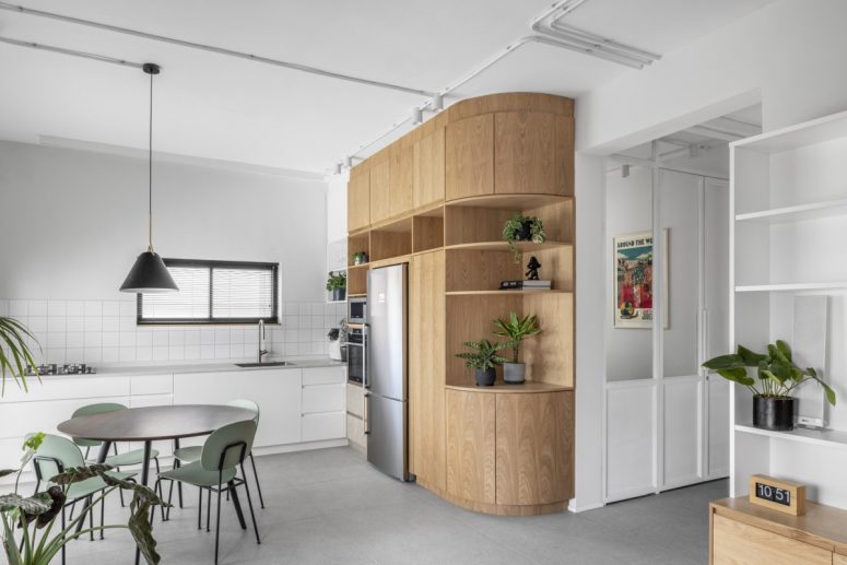 The kitchen, dining area and living room are combined into a large and open space with light gray flooring, white walls and oak furniture accents