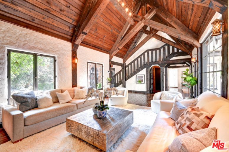 This barn living room is done with a wooden ceiling and beams, chic furniture and stone walls