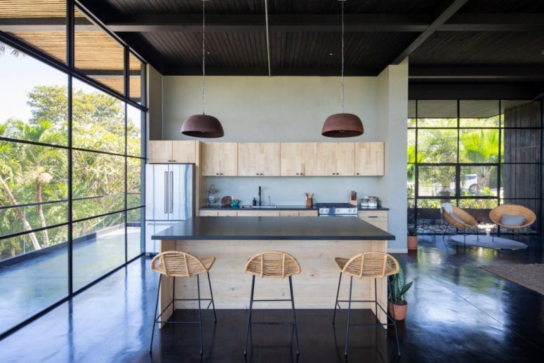 The kitchen is done with light-colored plywood cabinets, dark stone countertops and hanging lamps