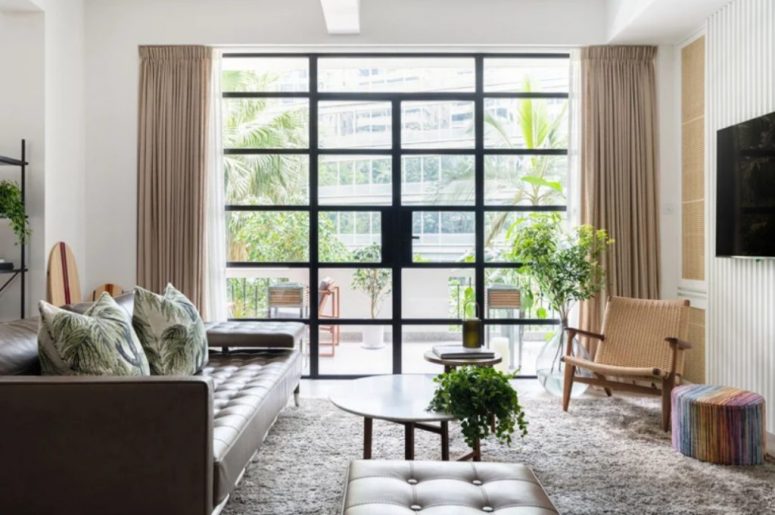 The living room is done with a leather sofa and ottoman, with a woven chair and a glazed wall that is an entrance to a terrace