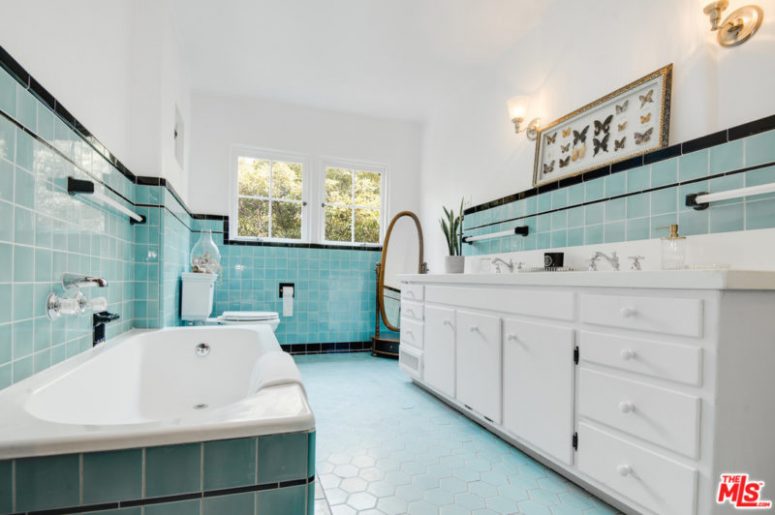 The bathroom is done with light blue tiles, a bathtub clad with tiles and a white vanity