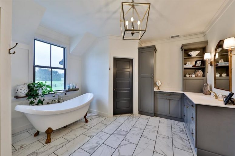The master bathroom is done with marble tiles, grey furniture, a clawfoot tub and cool views