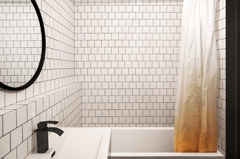 The bathroom is contemporary, with white tiles and black grout and more black accents for drama