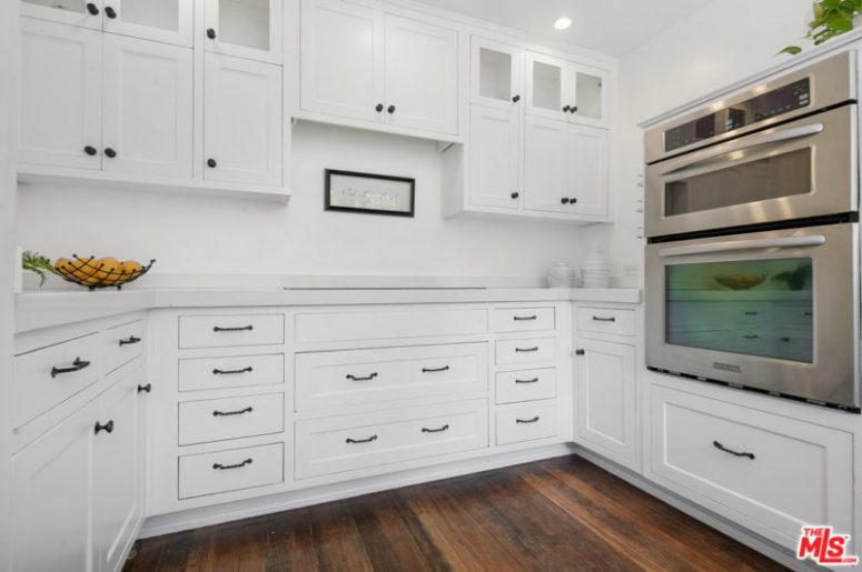 The kitchen is done in white, with chic traditional cabinets and black handles