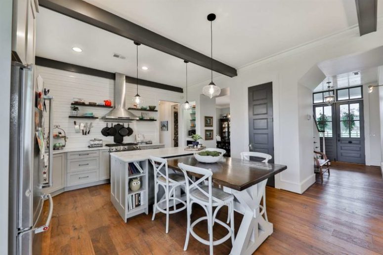 a white farmhouse kitchen design The kitchen is white, with a kitchen island and a trestle table that is attached to it for eating
