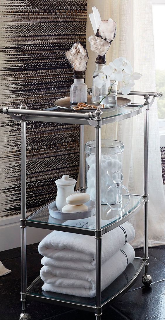 a refined stainless steel and glass rolling cart is a stylish storage piece with many items and some decor