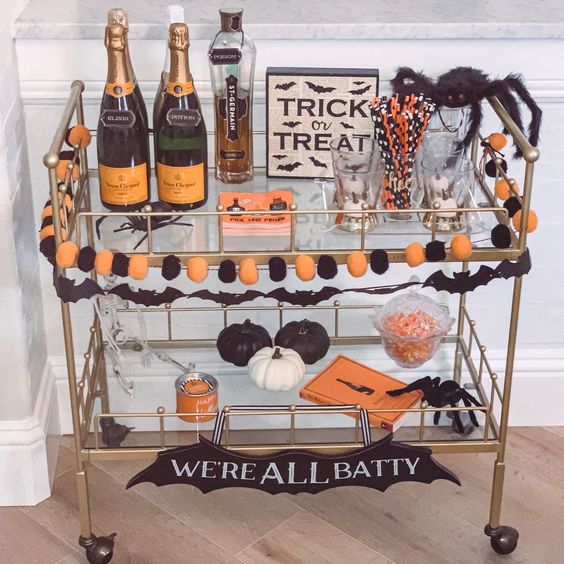 a bold Halloween bar cart with an orange and black pompom garland, black and white pumpkins, black spiders and drinks