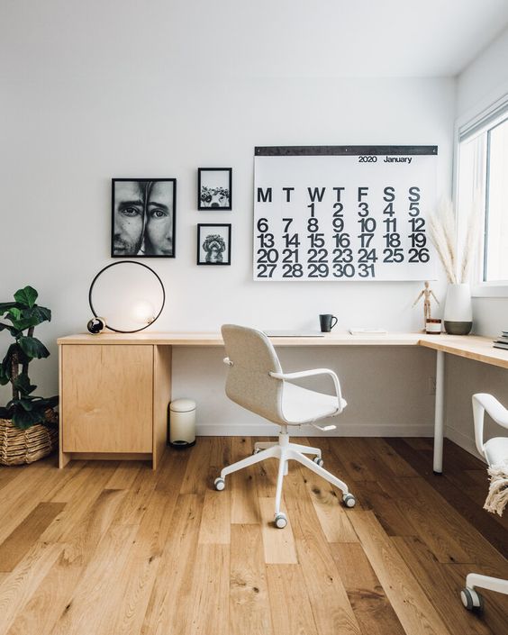 a chic Scandinavian home office with a large L-shaped desk, a white chair, some black and white artwork and decor on the desk
