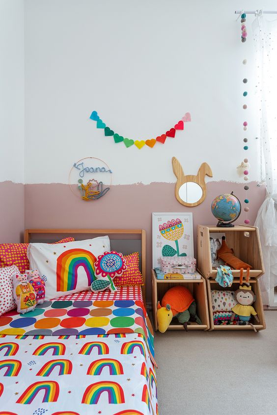 a colorful kid's room with a color block wall, colorful bedding and toys, bright garlands and a bunny mirror