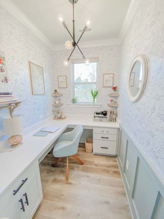 a cottage home office with printed wallpaper, mint paneling, an L-shaped desk, some decor and open shelves