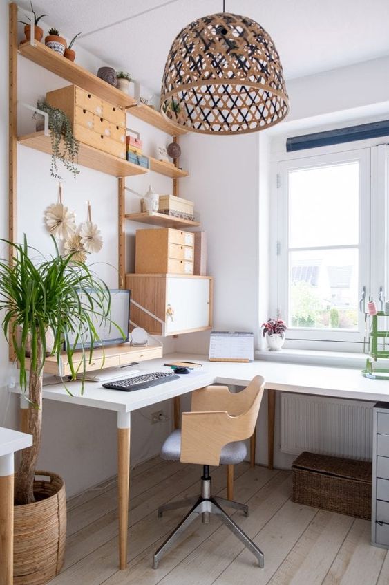 a creative Scandinavian home office with an L-shaped desk, a stained chair, open shelves and drawers, a pendant lamp