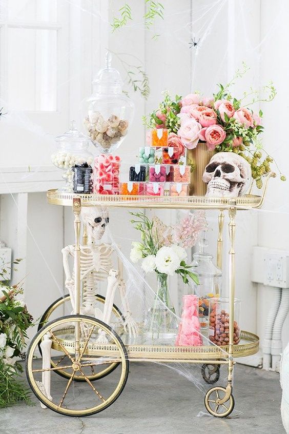 a cute glam Halloween bar with pastel blooms, skulls, a skeleton, lots of candies and sweets with much spiderweb