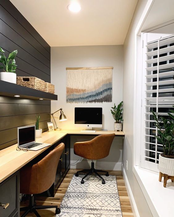 a farmhouse home office with a black planked wall, an L-shaped desk, a couple of leather chairs, potted plants and a macrame piece