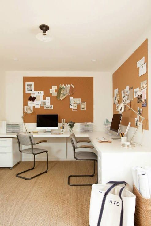 a home office with a large L-shaped desk, matching chairs, cork boards with decor and photos, table lamps and PCs