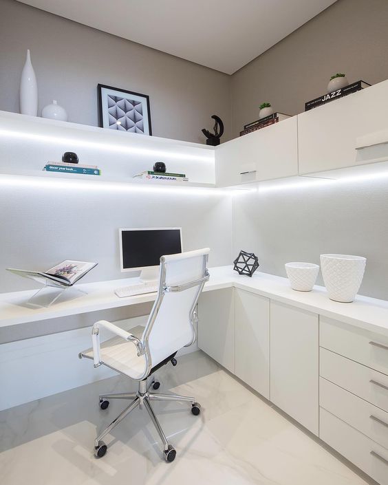 a minimalist home office with a corner desk and some storage cabinets under the surface, lit up shelves and cabinets above