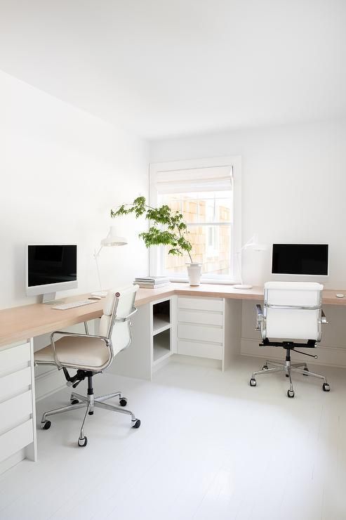 a minimalist white home office with an L-shaped desk, white chairs, storage units with drawers and potted greenery