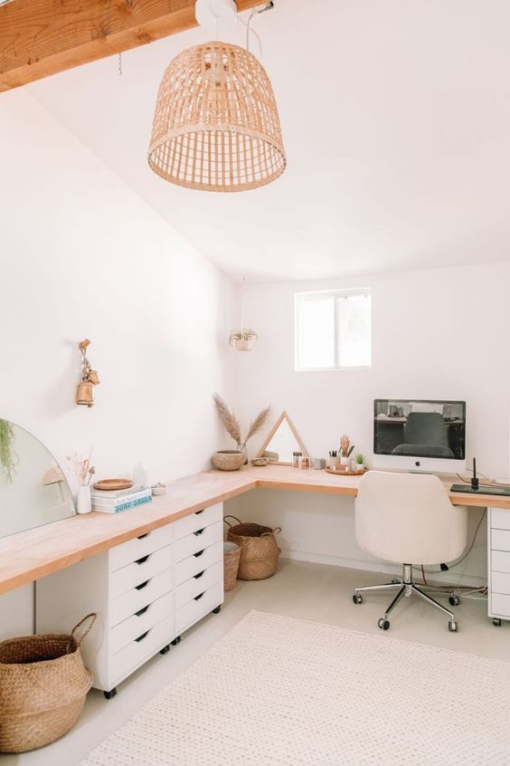 a neutral boho home office with a large L-shaped desk with some drawers, a white chair, some decor and baskets and a pendant lamp