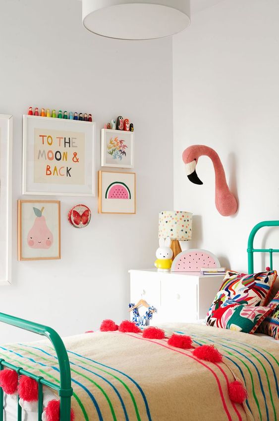 a pastel kid's room with pastel artworks, faux taxidermy, bright bedding and a bold green bed