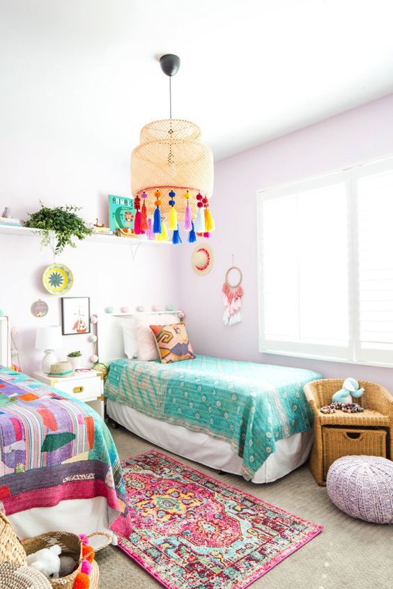a pastel shared kids' bedroom with lavender walls and a pouf, colorful bedding and art and a lamp with colorful tassels