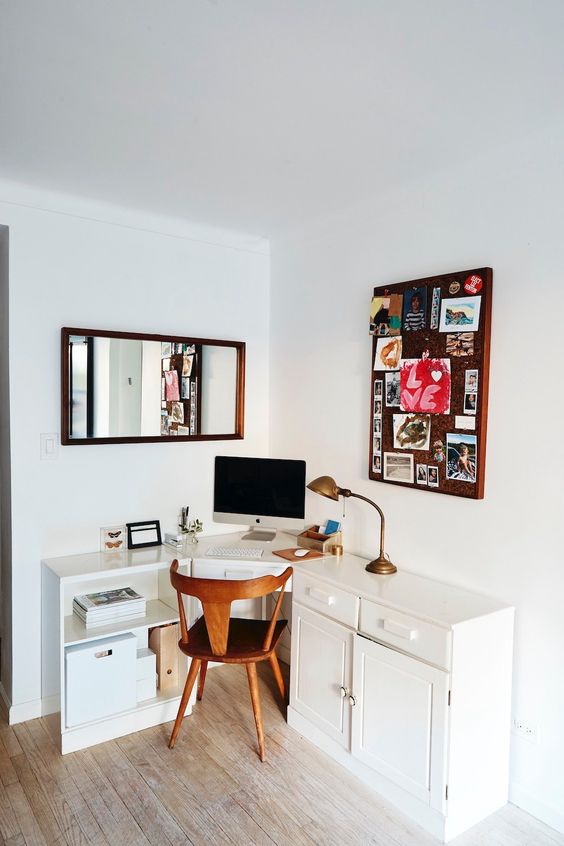 a small working space with a white corner desk, a stained chair, a memo board, a mirror and a vintage lamp