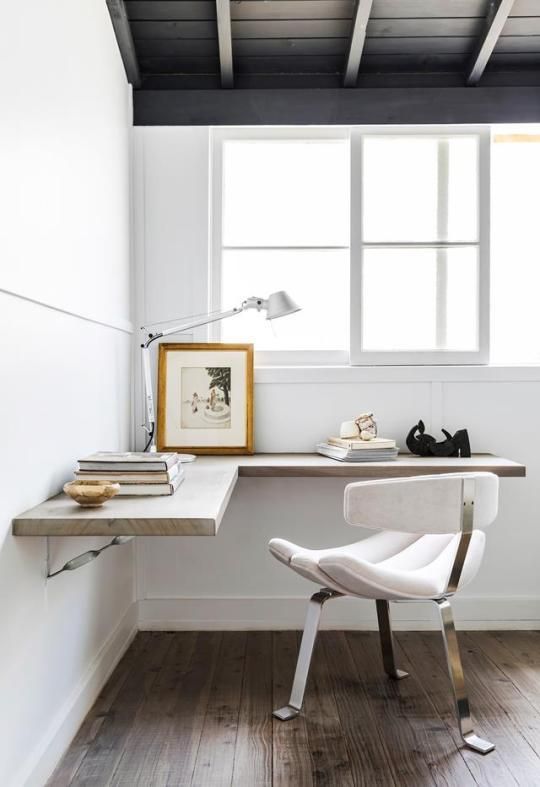 a stylish working corner with a floating L-shaped desk, a white chair, some decor and a table lamp is cool for working