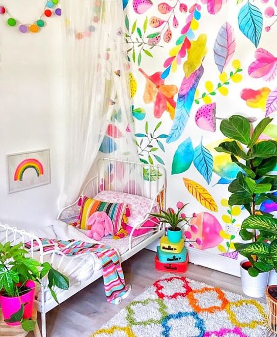 a super bright kid's room with a colorful botanical wall, bright bedding and a rug, colorful mini suitcases and a hot pink planter