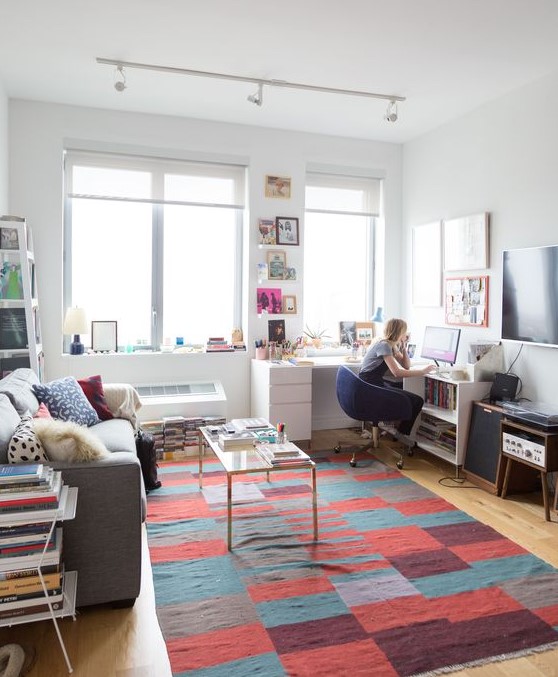 a vivacious living room with modern furniture, colorful art, books and a rug plus a corner desk for working there