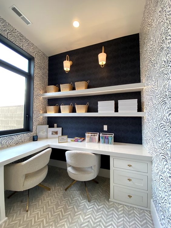 a whimsical home office with a black wall and printed wallpaper, a white L-shaped desk, white chairs, open shelves and some decor