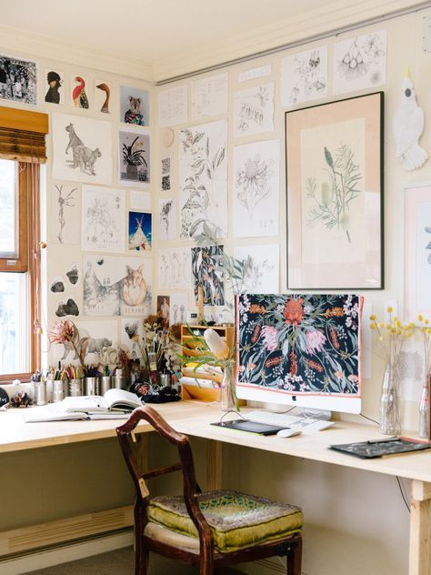 an art studio with an L-shaped desk and lots of art covering the wlals, a vintage chair and a PC