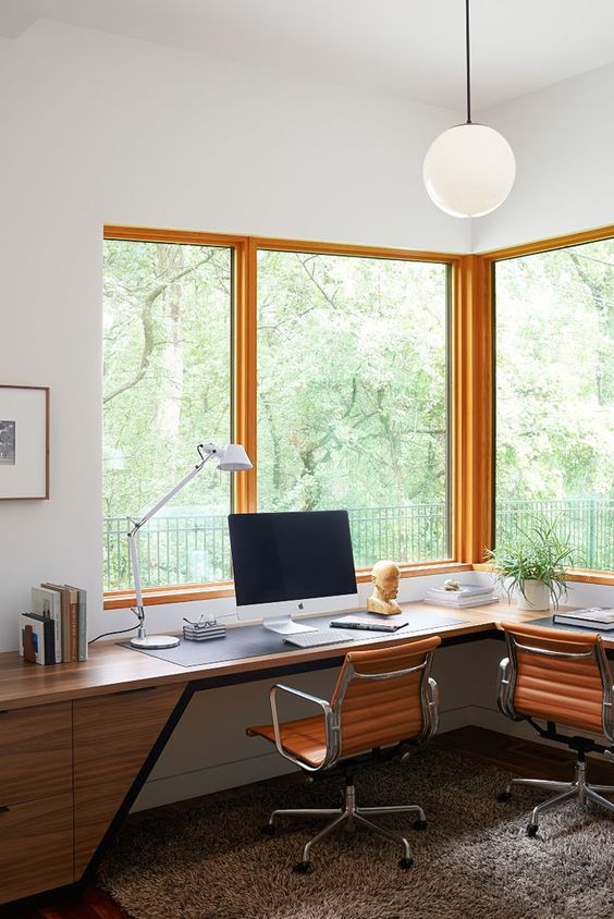 an elegant mid-century modern home office with a chic wooden corner desk, leather chairs and large windows to enjoy the views