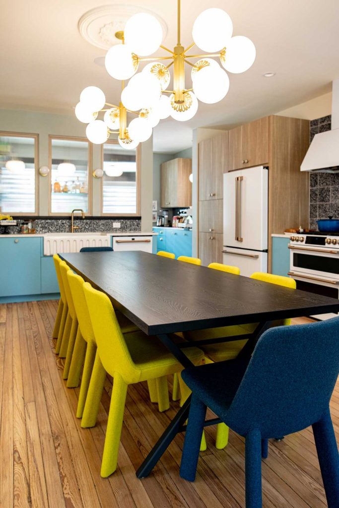 The eat-in kitchen shows off blue and white cabinets, a wooden dining table and yellow and navy chairs