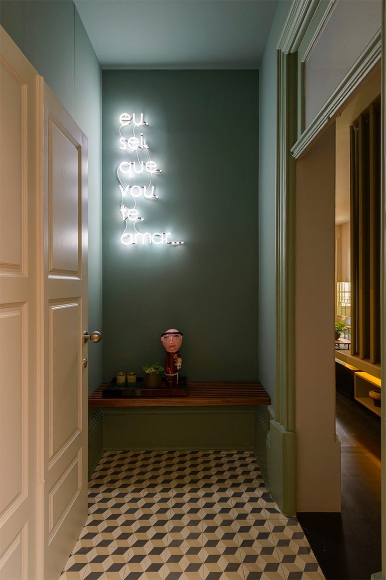 The entryway is done with green walls, a geometric floor, a bench and a neon sign and it looks bold and whimsy