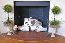 02 a fireplace clad with black matte tiles, with funny faux logs, topiaries on both sides and some pebbles