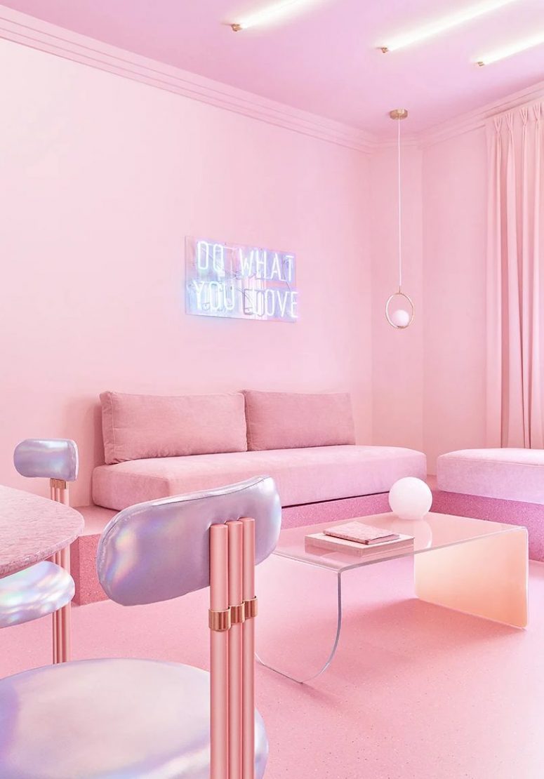 The living room is done with pink furniture put on pink stone, iridescent chairs, a neon sign, pendant lamps and an acrylic table, lights on the ceiling