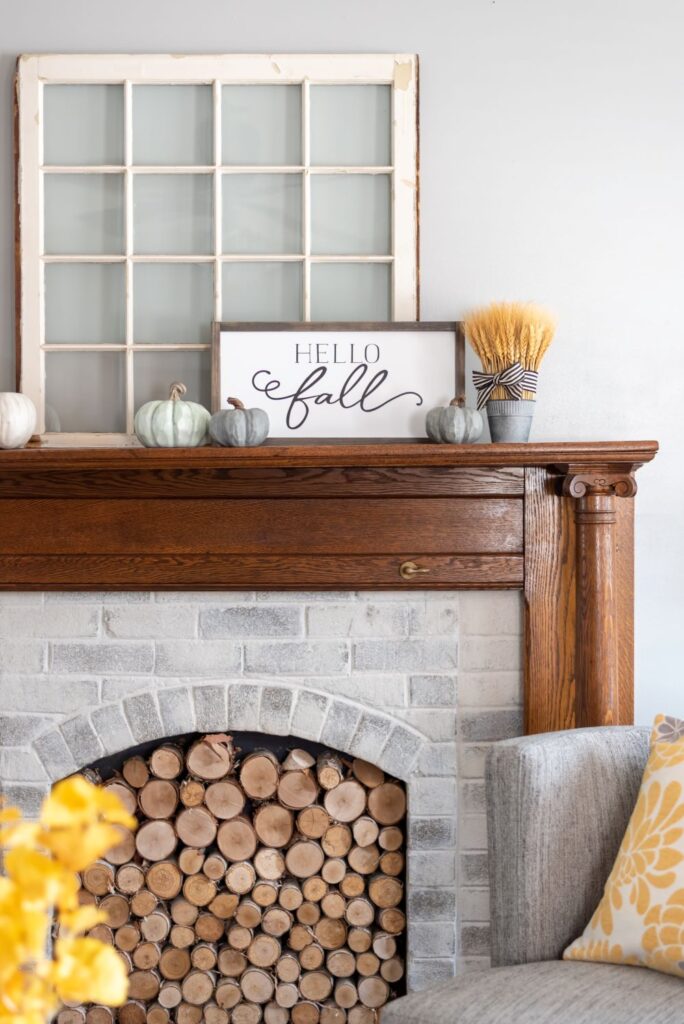 a farmhouse fireplace with a whitewashed brick surround, a stained wooden mantel and with firewood inside it