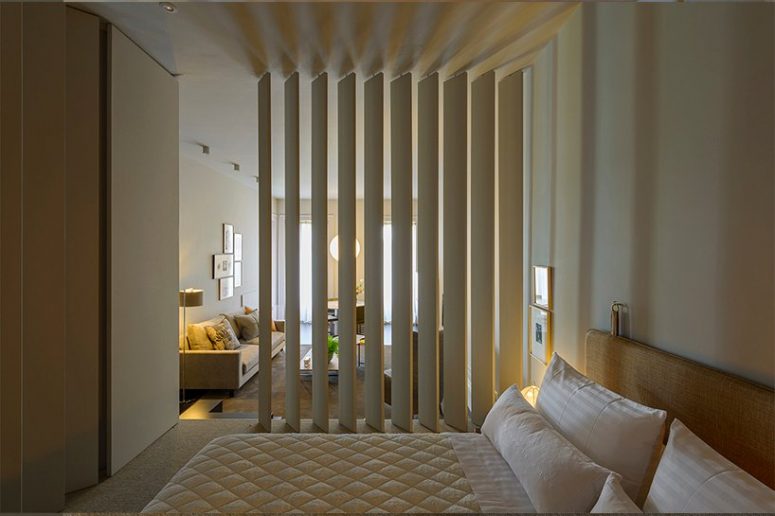 The bedroom is neutral, with white furniture, a large sleek wardrobe and some lamps and artworks