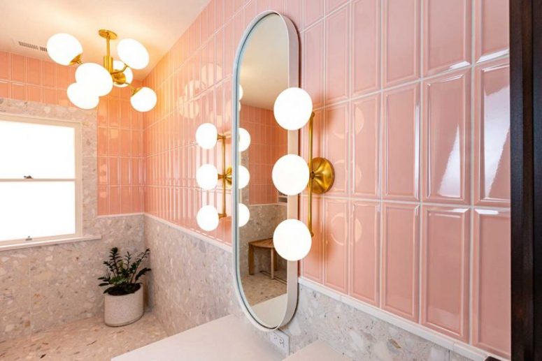 The bathroom is done with pink and terrazzo tiles, with retro lamps and a chandelier and a curved mirror