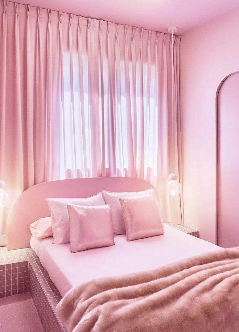 The bedroom is done in pink, with a pink bed on a tiled platform, pink and shiny pillows, a pink curtain and lights