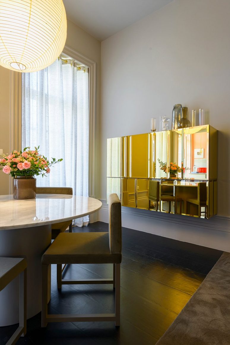 The dining room is very refined, with a round table with a marbel tabletop, chic chairs and a gorgeous polished gold cabinet on the wall