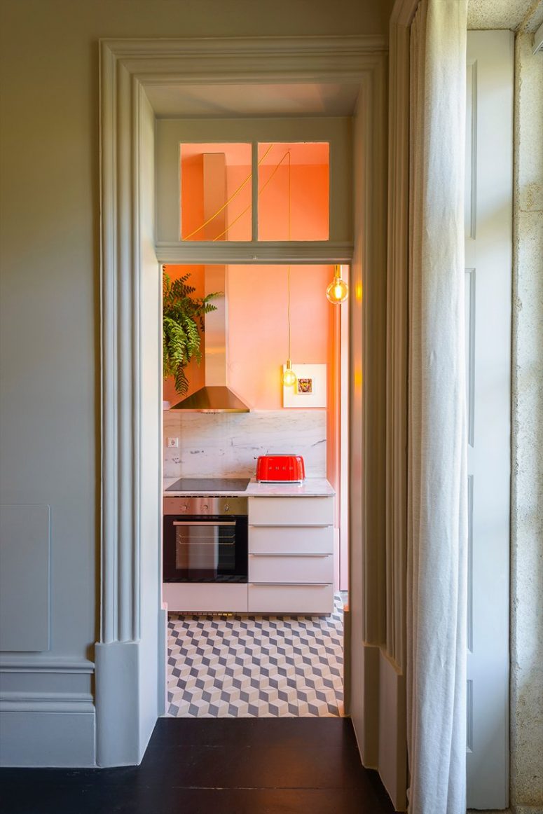 The kitchen shows off white cabinets, a white marble backsplash, peachy walls and greenery and pedant lamps