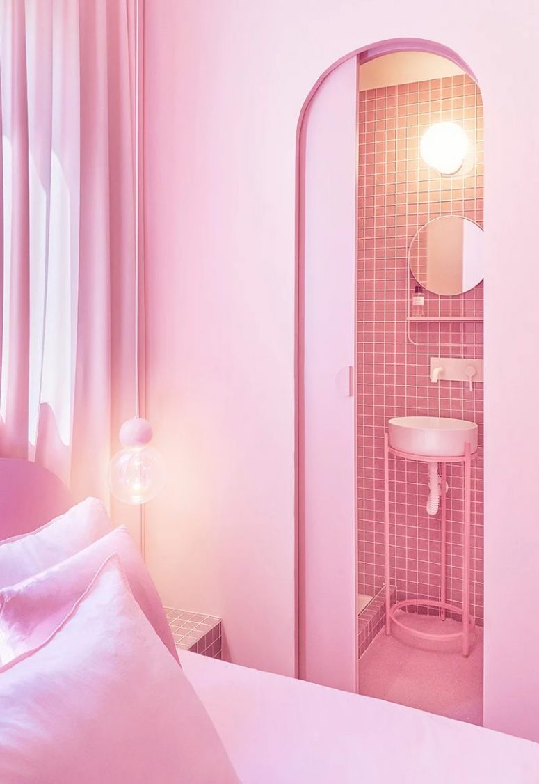 The bathroom is clad with pink tiles, and you may see a small round mirror and a sink on a stand